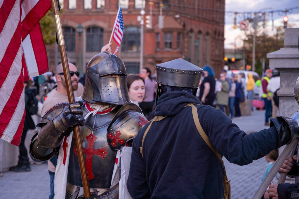 Two individuals dressed as knights, one protesting the president, one supporting, pass each other in Clinton Square at the Trump rally protest on October 9, 2026.