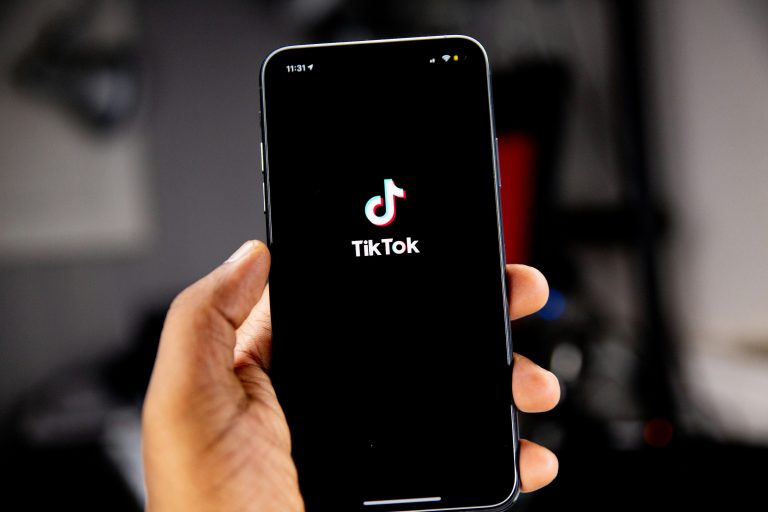 Brown-skinned hand holding a phone with the TikTok app open.