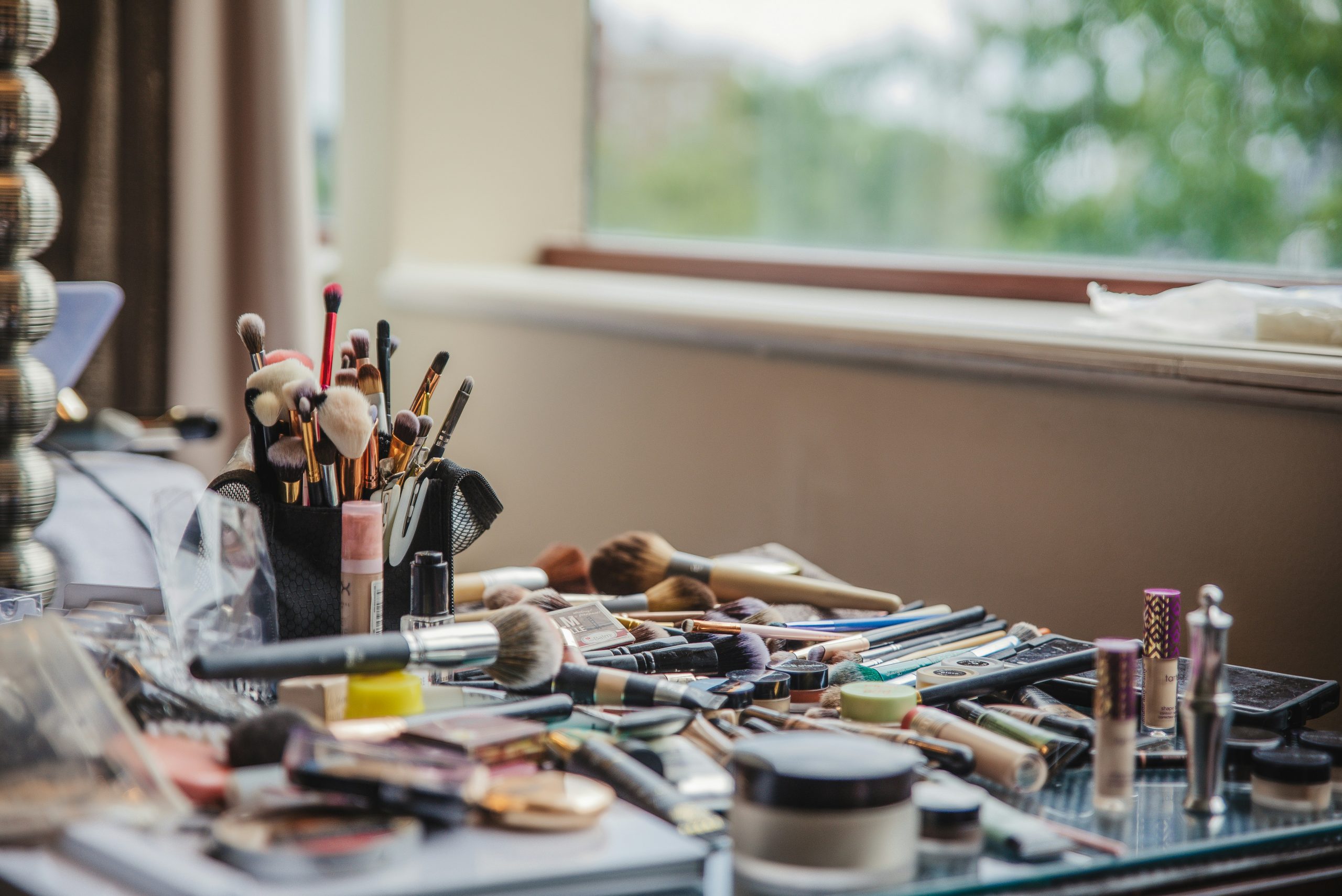 Beauty and makeup supplies on a desk by teh window.