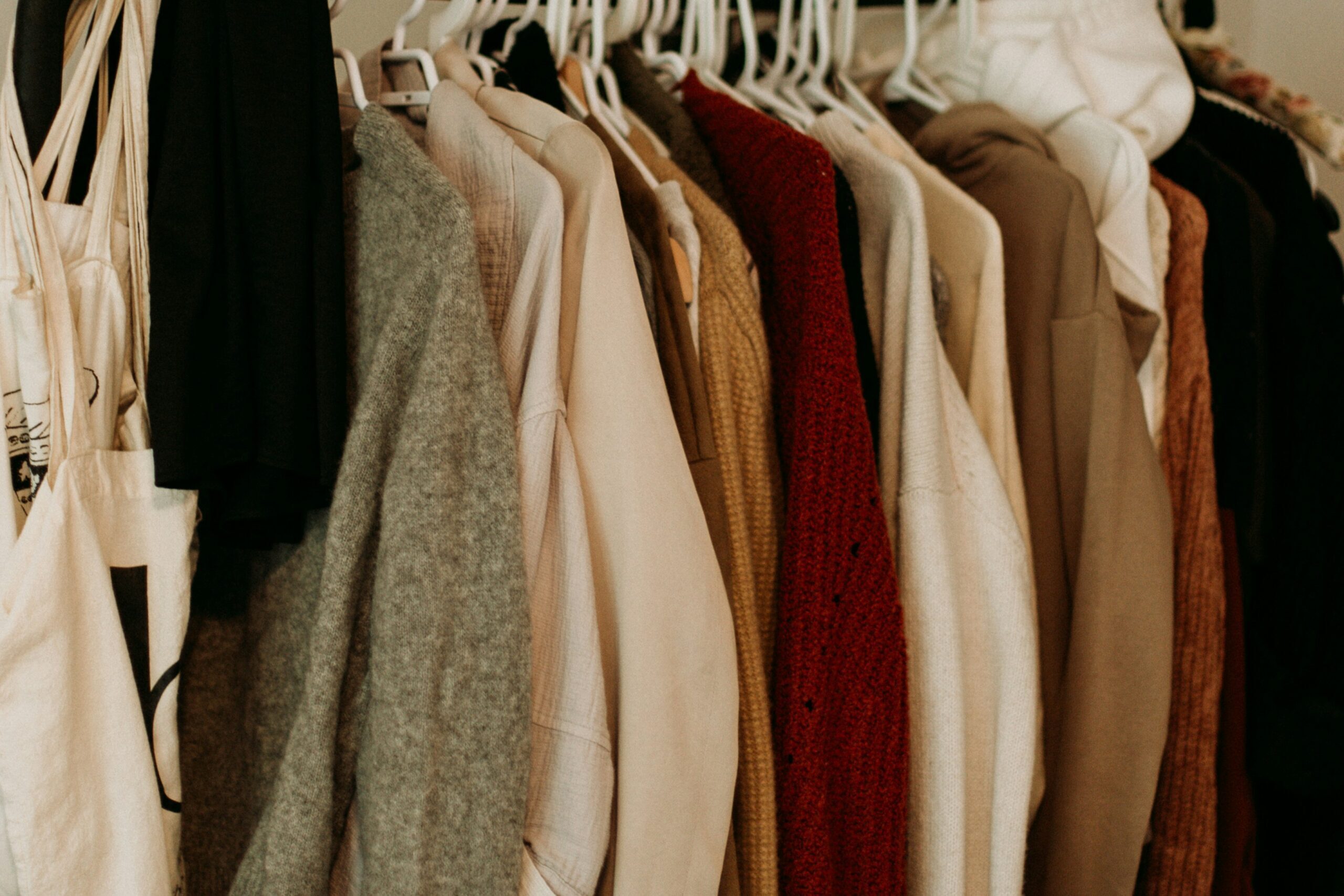 On a clothing rack an array of neutral-colored sweaters hang.
