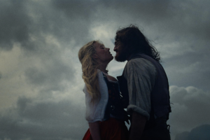 In "Wuthering Heights" against a grey sky, a woman with blonde hair and a shaggy man stand close to each other.