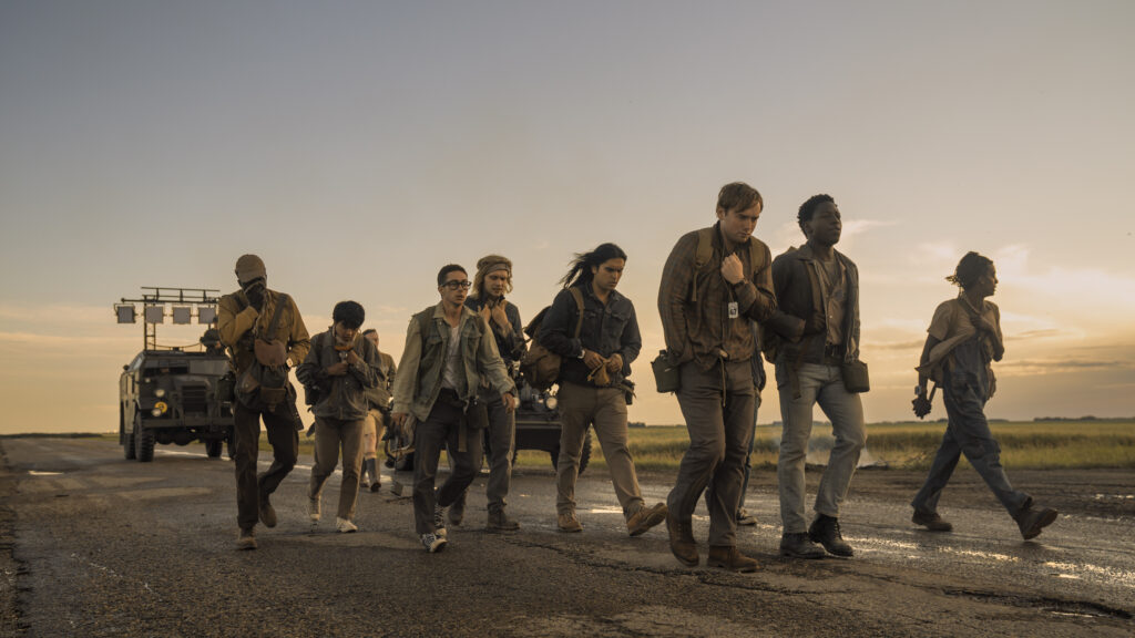 Teenagers walking down a road in a sunset with a tank following them in the distance