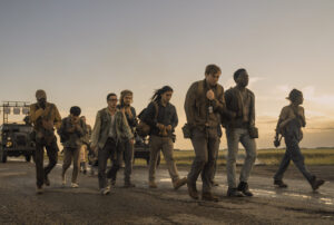 Teenagers walking down a road in a sunset with a tank following them in the distance