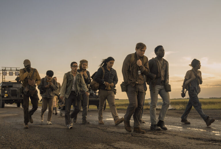 Teenagers walking down a road in a sunset with a tank following them in the distance