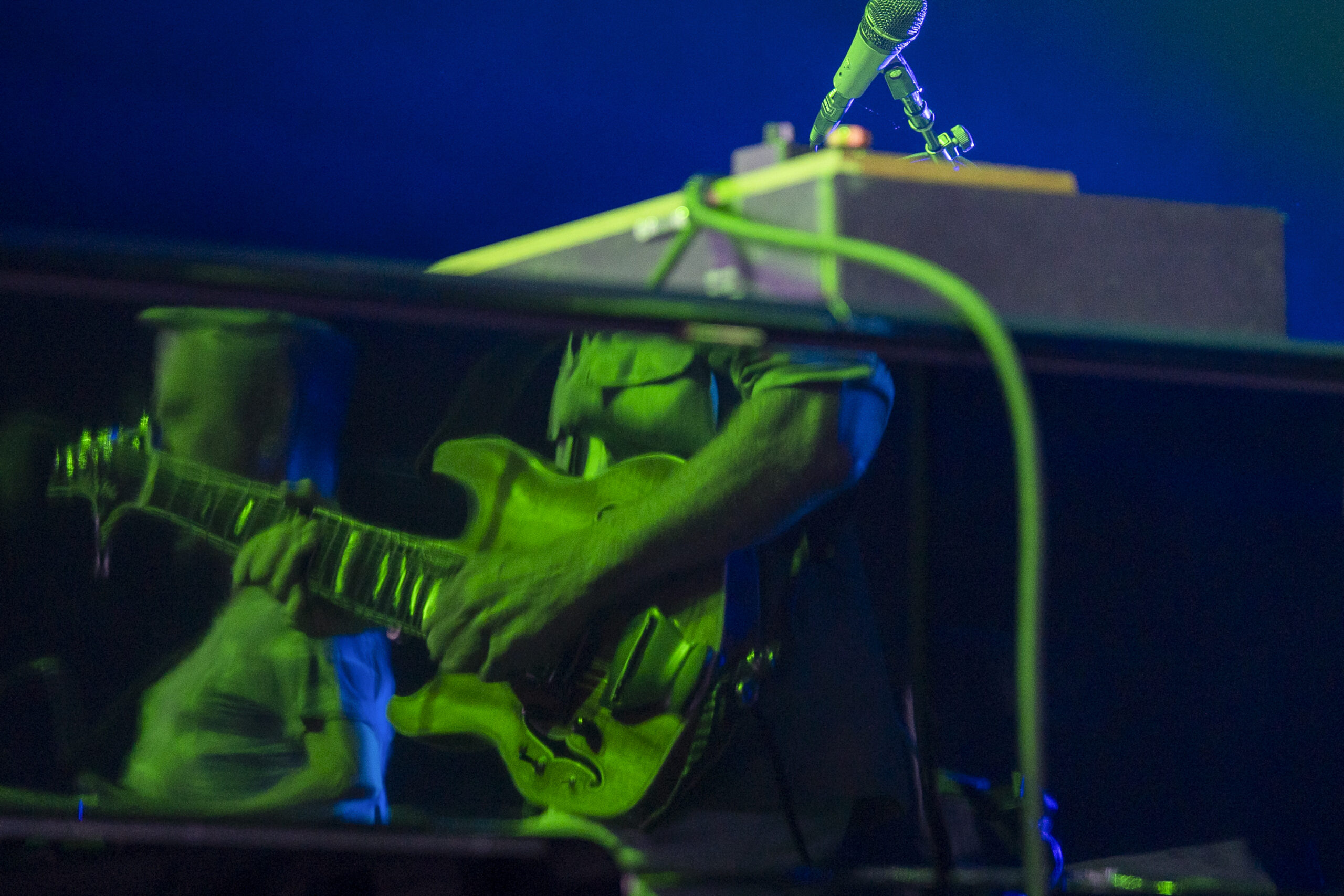 Guitarist Trey Anastasio is reflected in the glossy surface of Page McConnell’s piano as McConnell performs at the top right of the frame during Phish’s concert at Empower Federal Credit Union Amphitheater at Lakeview in Syracuse, N.Y., on Tuesday, July 21, 2026. The layered image mirrors the close interplay between Anastasio’s guitar and McConnell’s piano, organ and synthesizer work during the band’s extended improvisations. Photo by Matt Hofmann