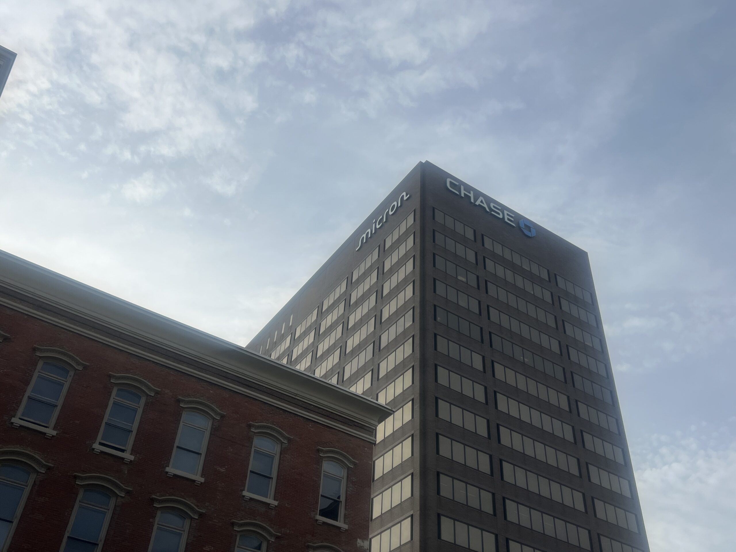 A tall grey building lined with windows stands tall against a blue sky in a downtown city.